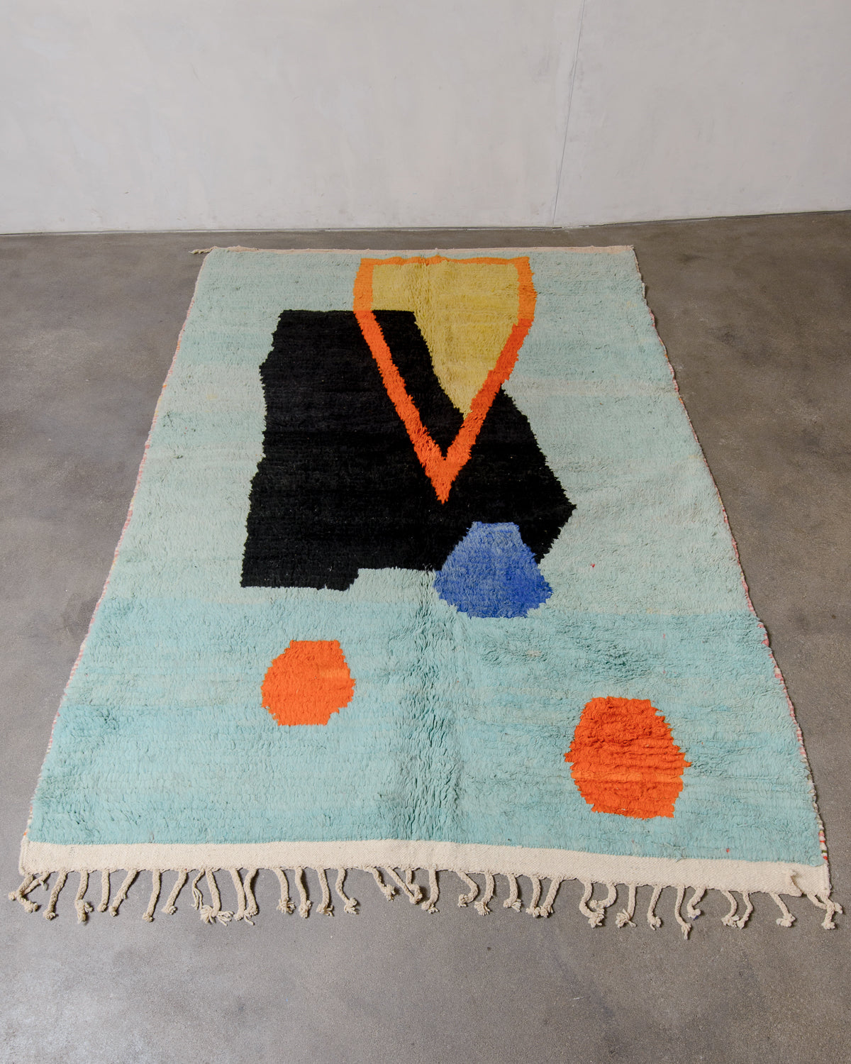 Berberlin vintage Berber rug made of colourful wool laying flat on a concrete floor.